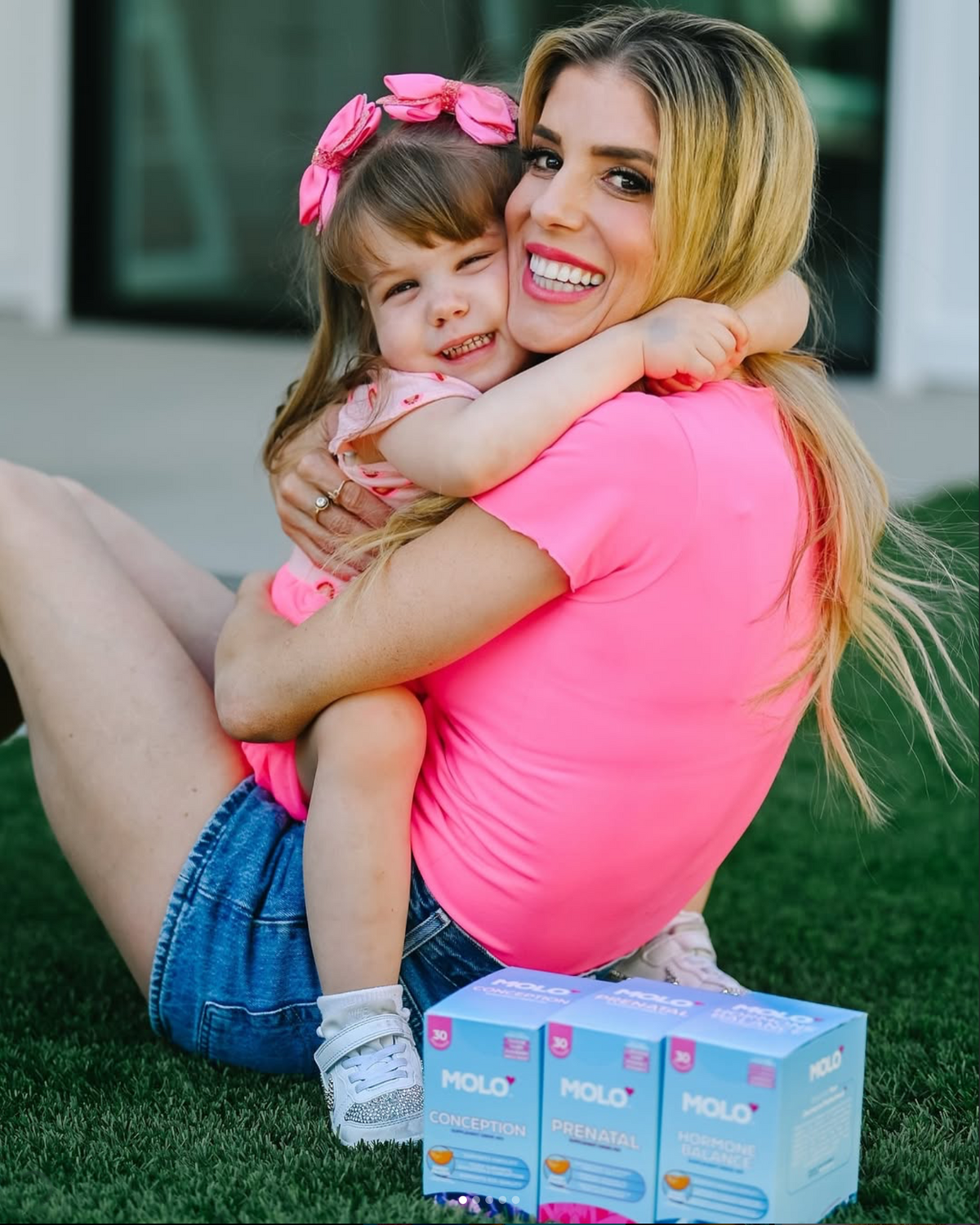 Rebecca Zamolo sitting on the grass hugging her daughter, with Molo cartons beside them