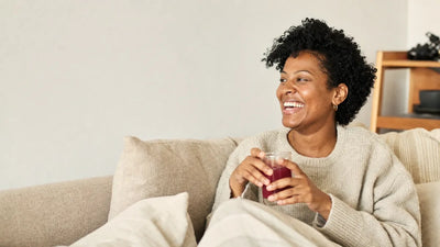 A woman laughing on her sofa, holding a glass of a deep red drink