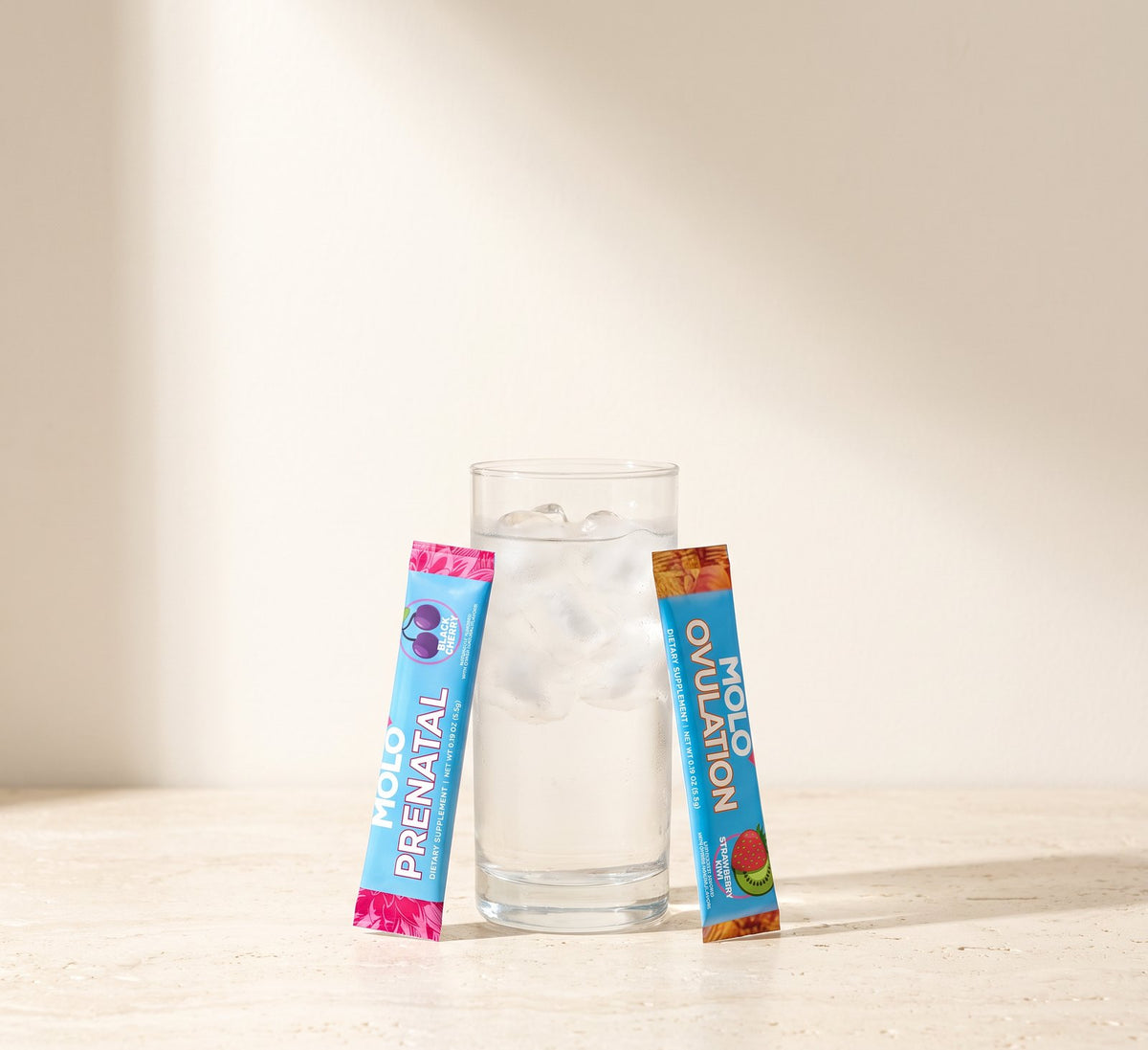 A Molo Prenatal stick and a Molo Ovulation stick leaning on either side of a glass of ice water